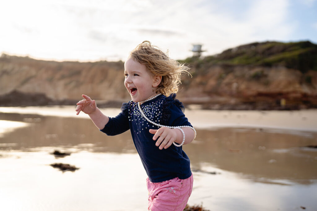 Child running along the beach in playful outfit with wind in her hair