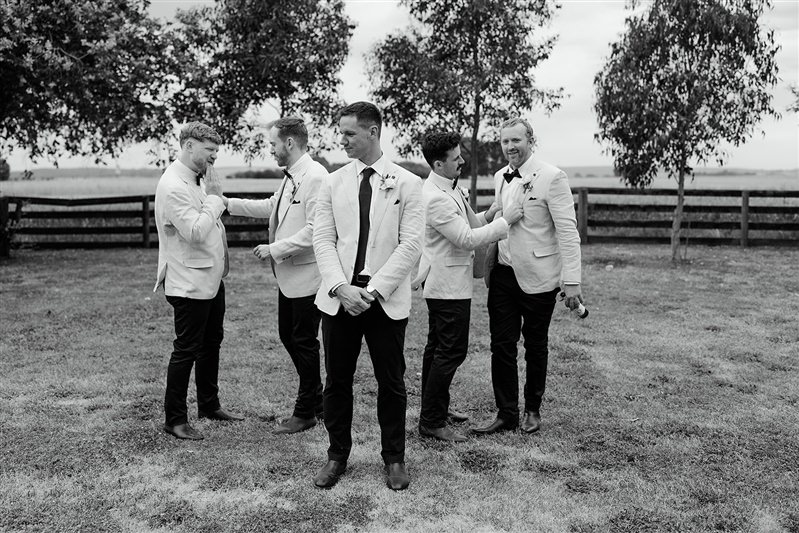 Black and white photo of groomsmen walking through paddock