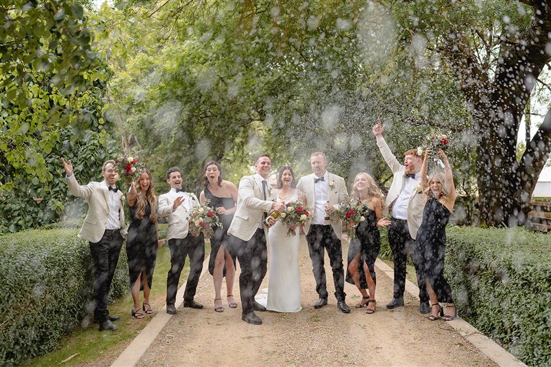 Group champagne spray celebration with bride and groom laughing