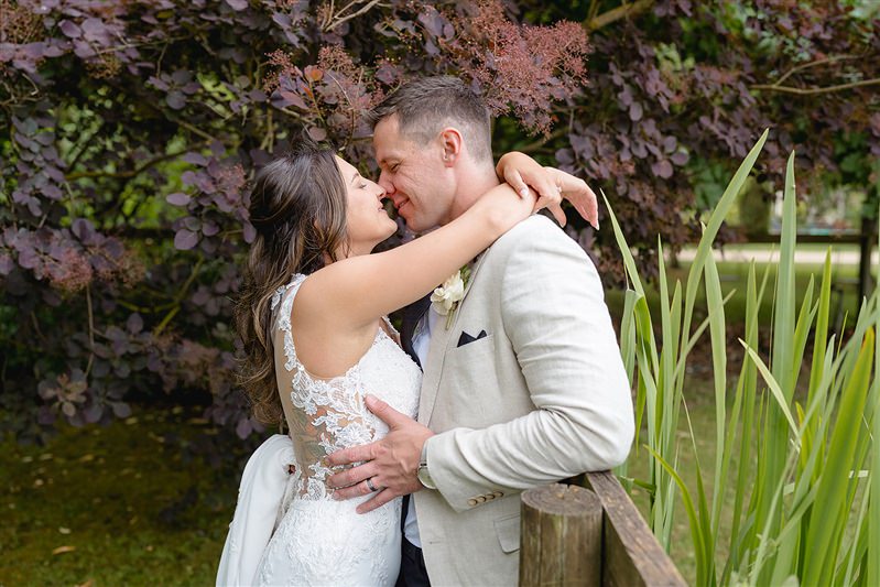 Bride hugging groom tightly with greenery behind