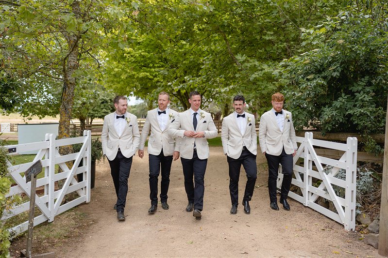 Groomsmen walking in formation near white timber fence