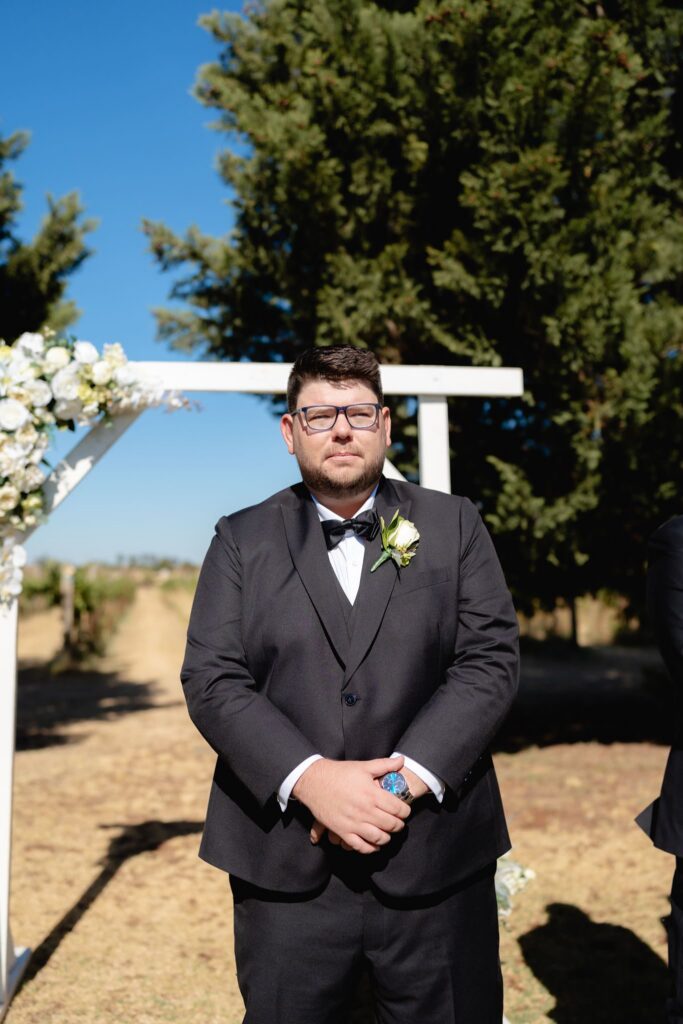 Groom waiting at the ceremony arch at Witchmount Estate wedding by the vines
