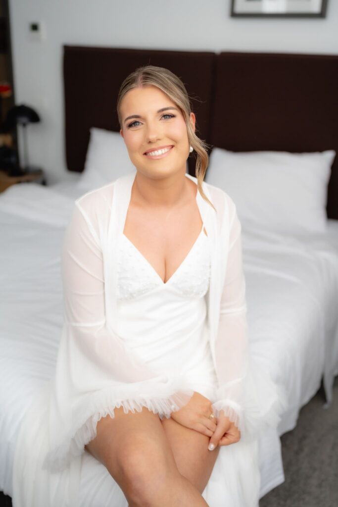 Bride in a robe seated on the bed before Botanic Gardens and Industry26 wedding